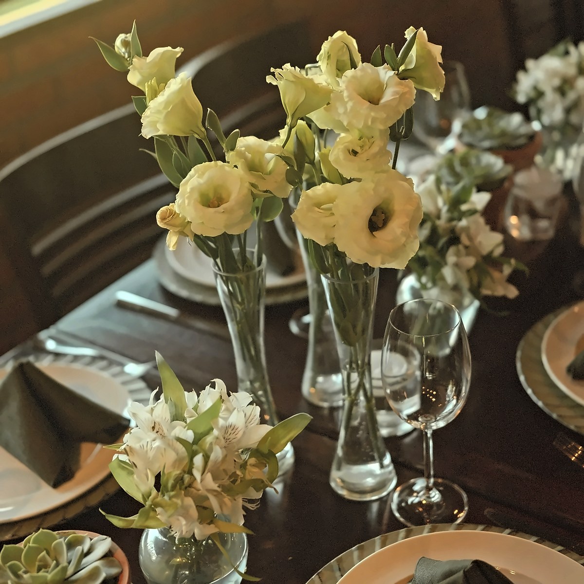 Arranjos de mesa para jantar com lisianthus brancos e alstroemérias em jarras de vidro e suculentas em vasos de barro, pela Florabella em Fafe
