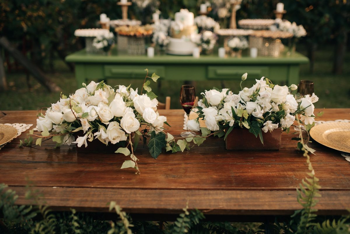 Arranjos baixos de rosas brancas, alstroemérias e hera em caixas de madeira numa mesa rústica de casamento, pela Florabella em Fafe