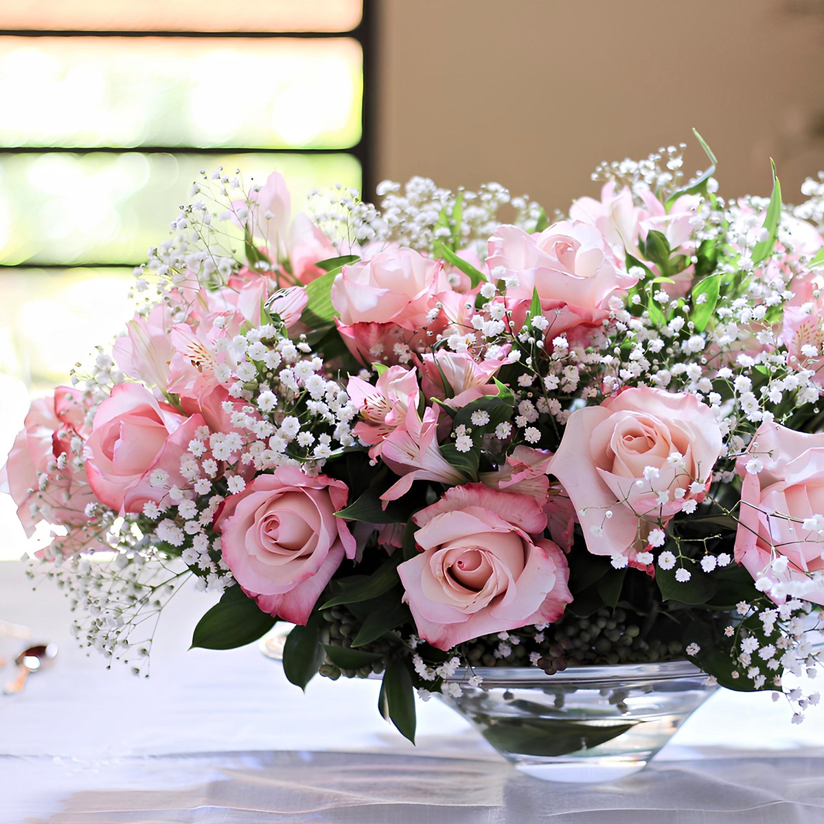 Centro de mesa com rosas cor-de-rosa, alstroemérias e gipsófila numa taça de vidro, para festa ou evento, pela Florabella em Fafe