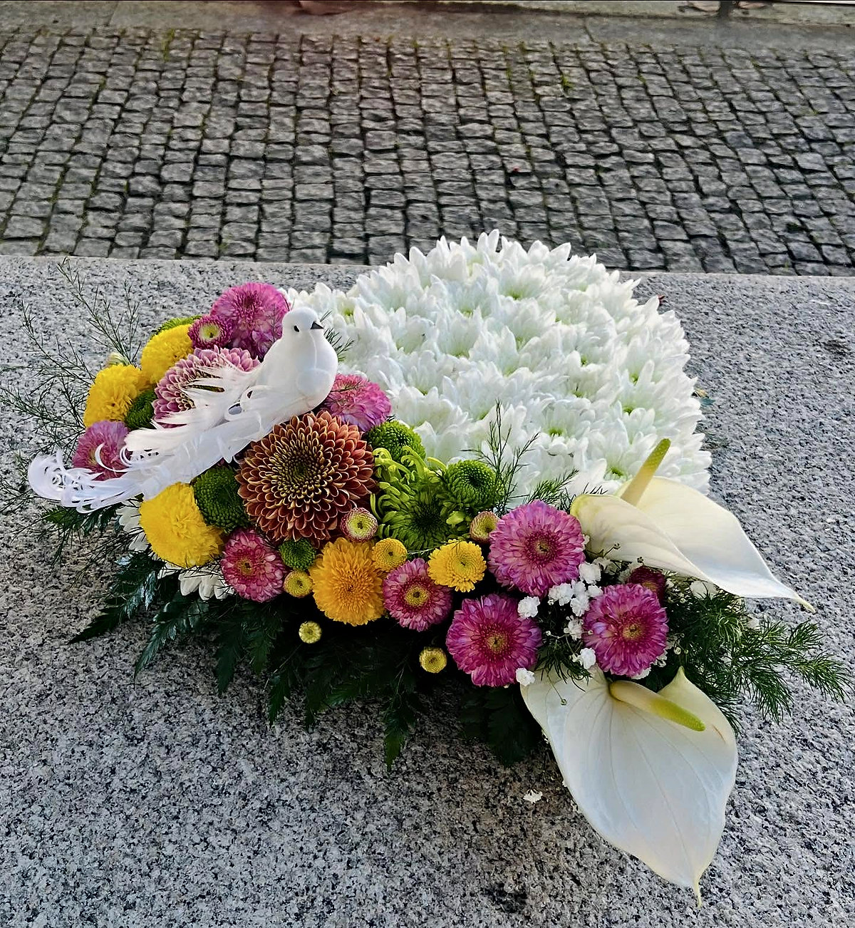 Coração de crisântemos brancos com pomba branca, antúrios e crisântemos cor-de-rosa, amarelos e verdes, feito pela Florabella em Fafe