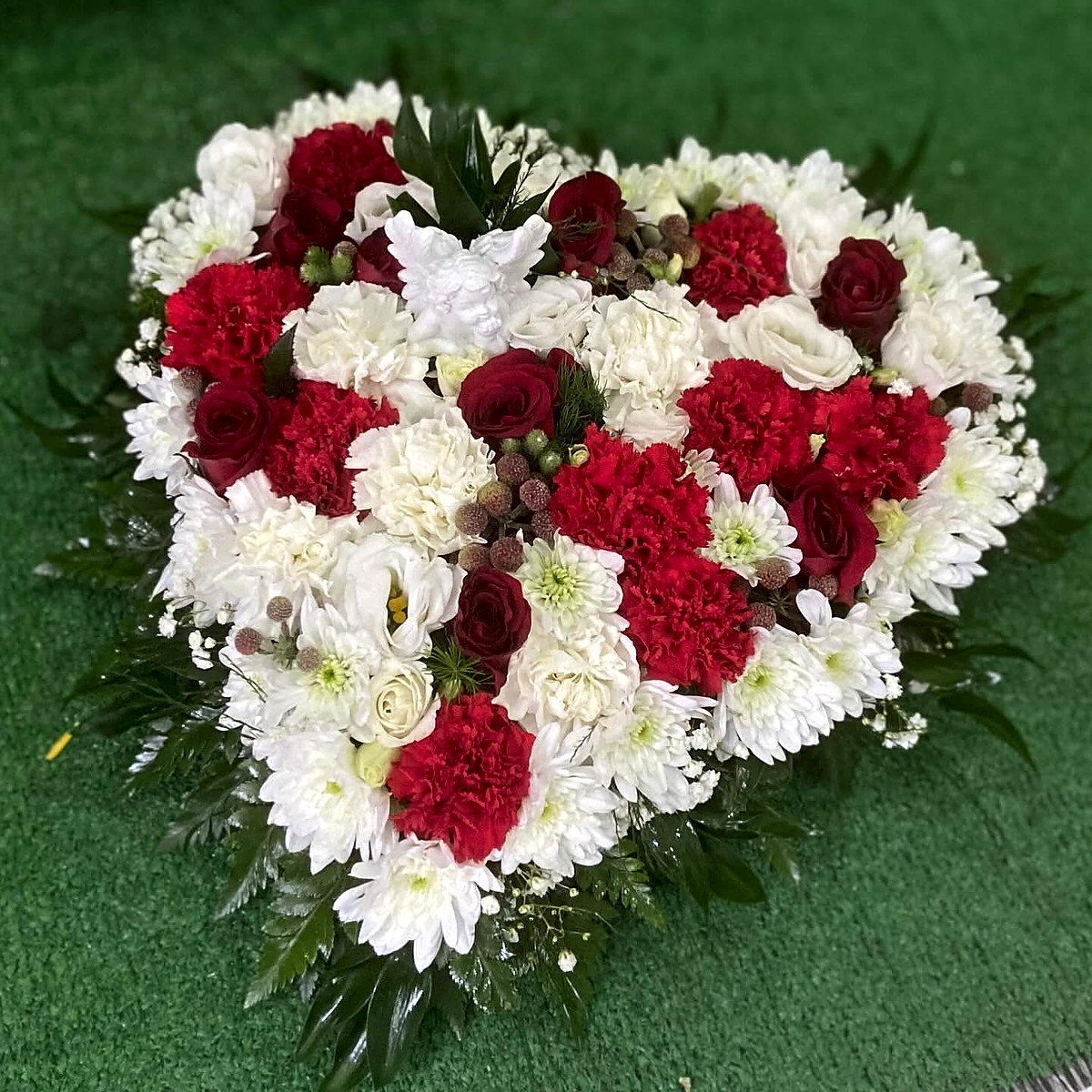 Coração de flores para funeral com cravos e rosas vermelhas, crisântemos e cravos brancos, lisianthus e anjo decorativo, feito pela Florabella em Fafe