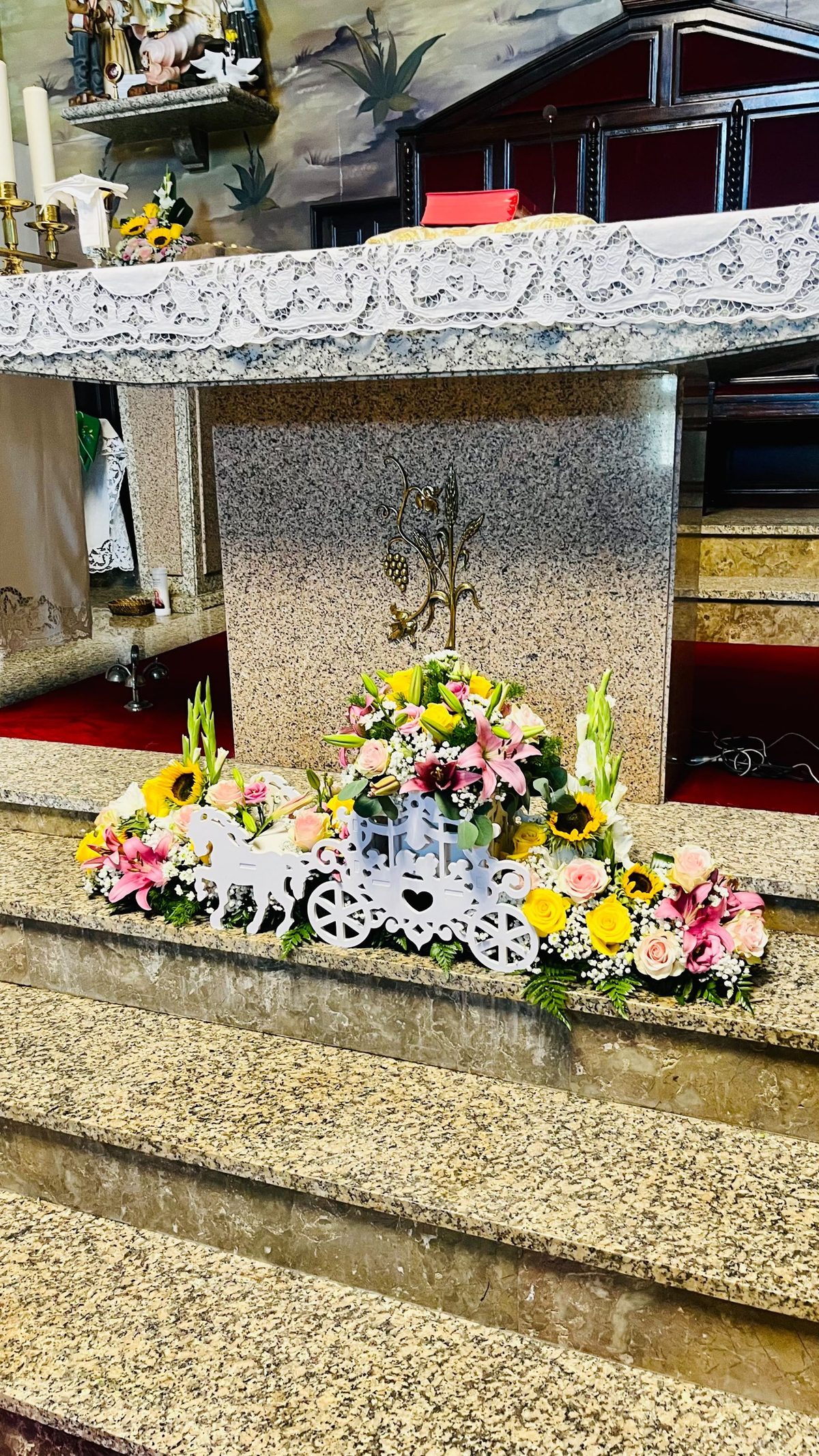 Decoração floral do altar para batizado com carruagem branca, girassóis, lírios cor-de-rosa, rosas e gladíolos, pela Florabella em Fafe