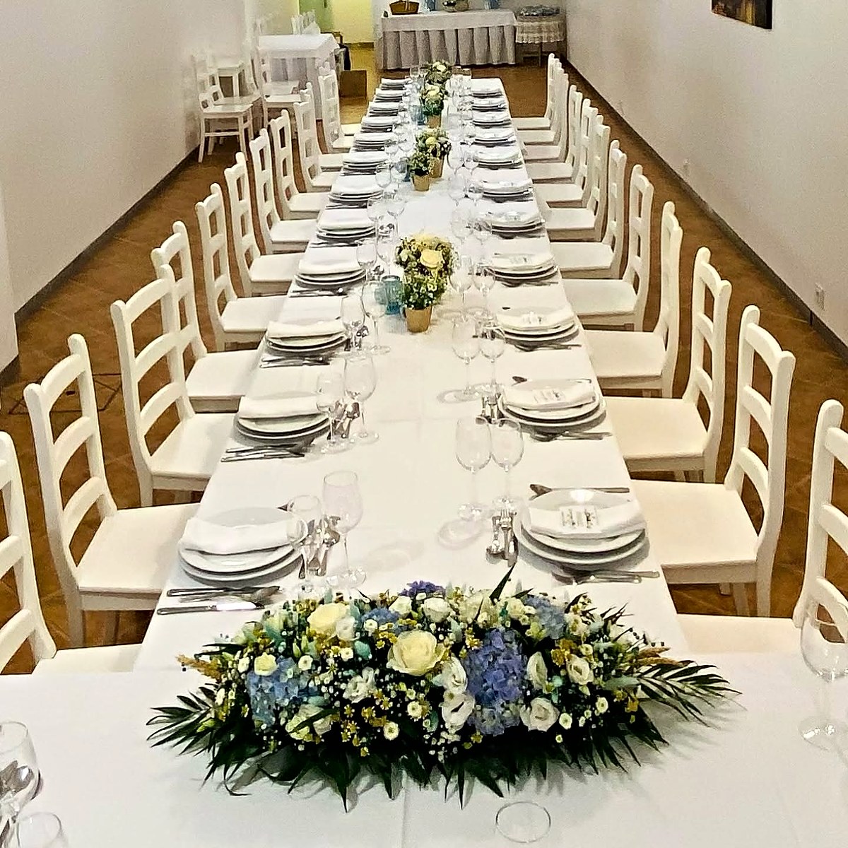 Mesa comprida de jantar de festa com centros de mesa de hortênsias azuis, rosas brancas e lisianthus, pela Florabella em Fafe