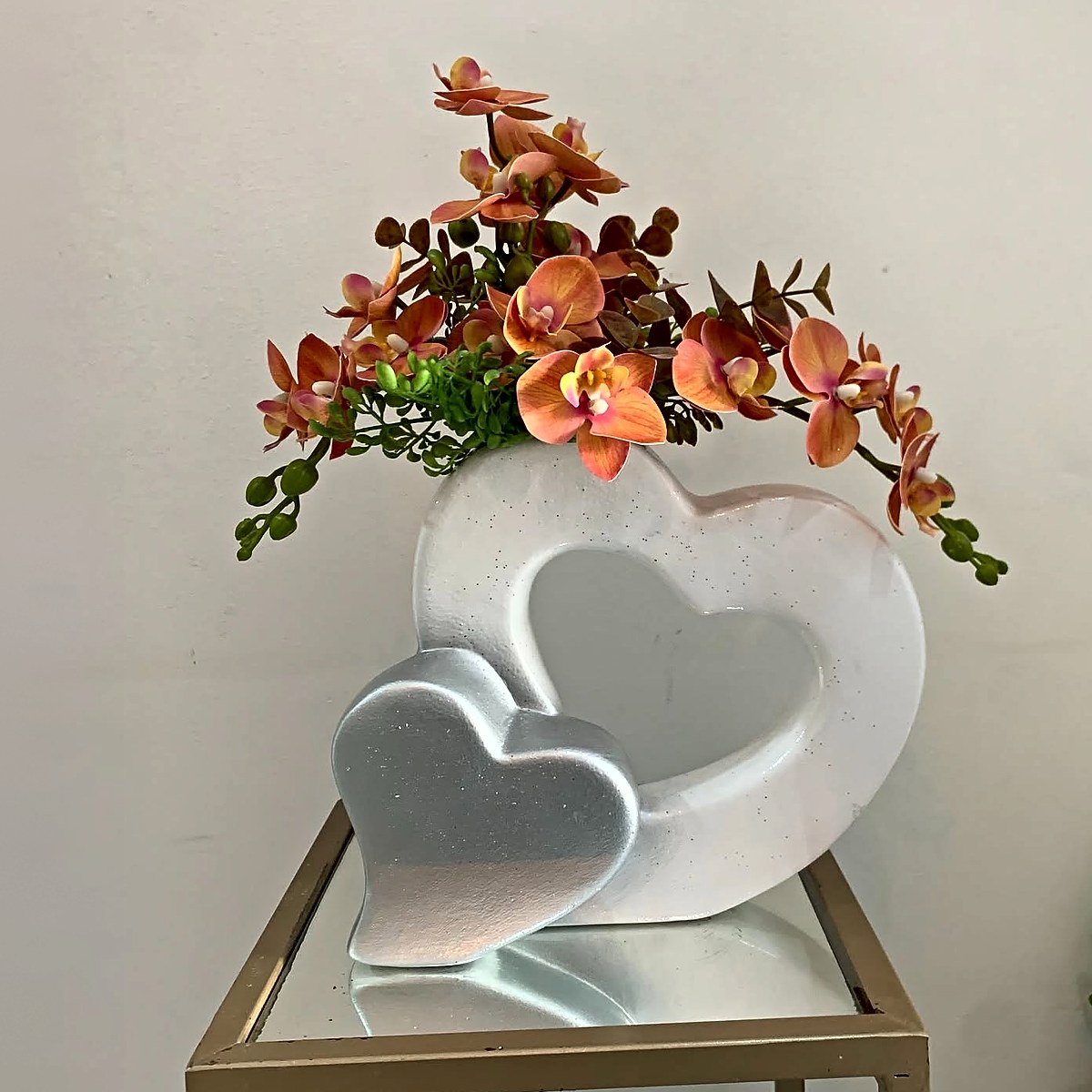 Orquídeas cor de laranja num vaso branco em forma de coração com coração prateado, peça de decoração da Florabella em Fafe