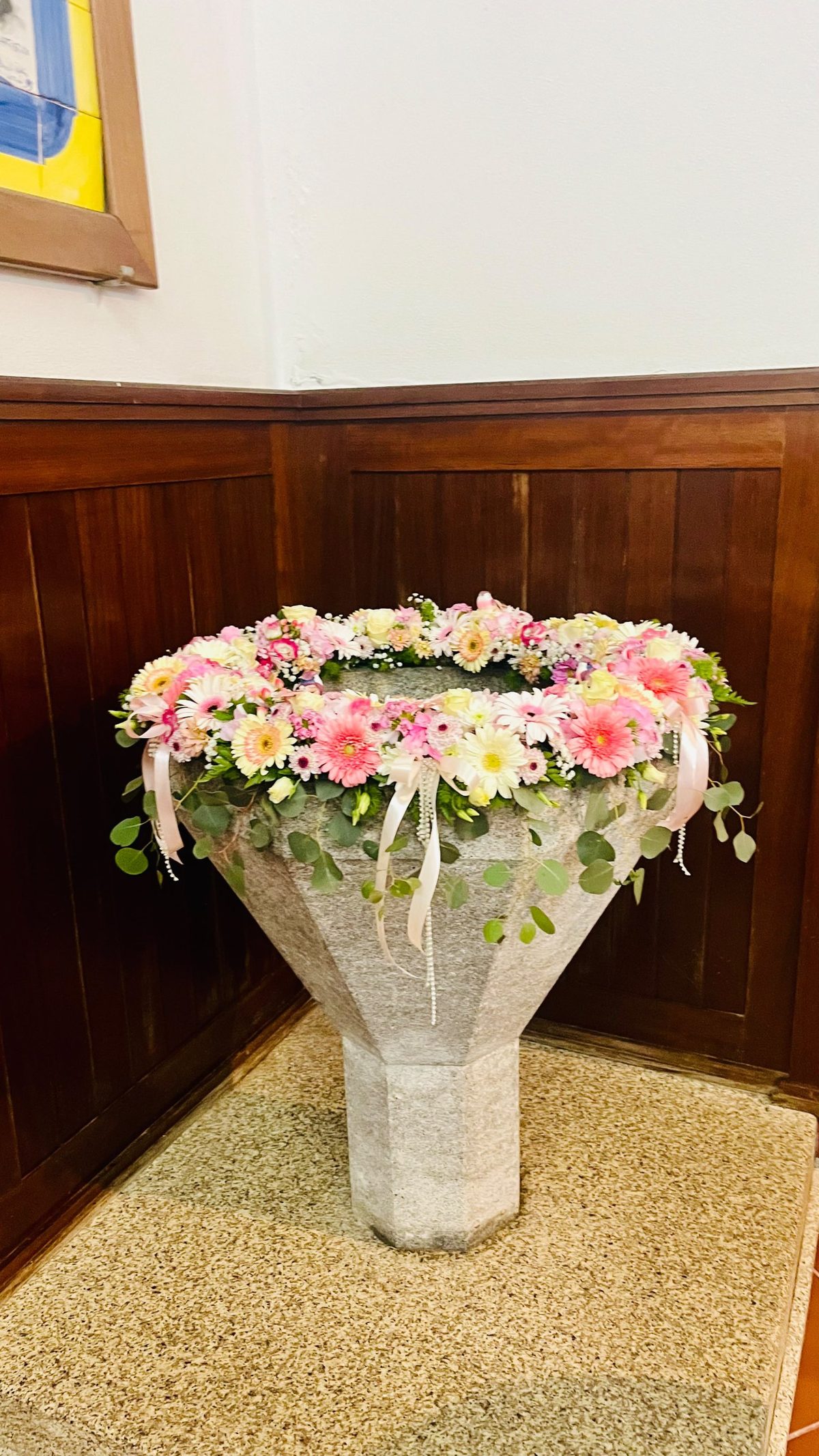 Pia batismal de granito decorada com uma coroa de gérberas, rosas, hortênsias e eucalipto para batizado, pela Florabella em Fafe
